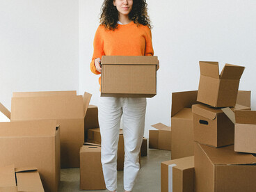 A young woman settles into a new space, surrounded by cardboard boxes during relocation