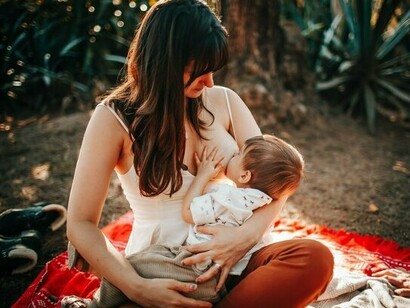 A mother breastfeeding her infant in the warmth of the outdoors, representing the nourishment, protection, and connection provided by human milk