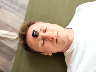 A practitioner places a healing crystal on a man’s forehead, channeling energy through reiki for inner balance