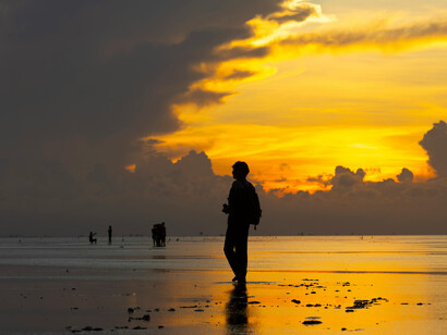A man walking along the beach at sunset, silhouetted against the sky