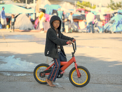 Niño con una bicicleta en un campamento de migrantes en la frontero de Tijuana, México