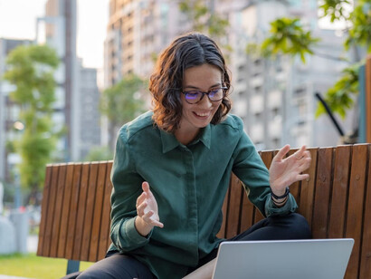 A young woman smiles during a video call from a park bench — still hopeful, even as unpaid work blurs the line between opportunity and exploitation