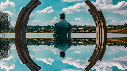 A man's self reflection, framed by a sculpture and the sky
