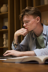 A young man studies in a virtual classroom and in a library, focusing on academic writing