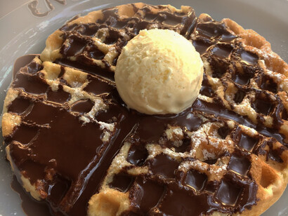 Breakfast waffles covered in chocolate with a scoop of vanilla ice cream