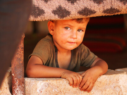A young child in a Syrian refugee camp stares solemnly into the camera, one of many caught in the crossfire of a fractured nation and a fading Kurdish dream