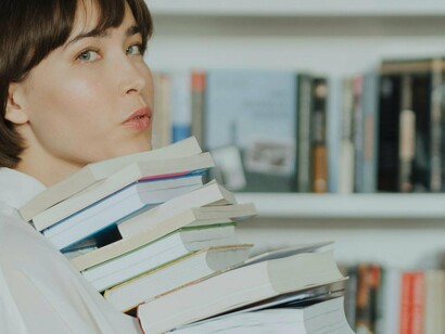 Mulher carrega suas próximas leituras. A narrativa torna-se assim, uma condição da experiência prática, pois o próprio campo da práxis humana é sempre narrativamente pré-figurado, quer dizer, está sempre articulado por meio de signos, regras, costumes, valores que permitem que as pessoas se entendam ou divirjam na constituição da sua identidade