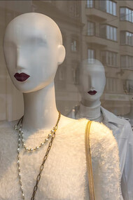 A white human skull wearing a yellow shirt displayed in the window of a luxury fashion store.