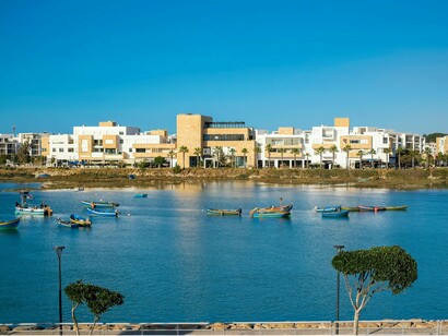 Painted boats going across the blue waters of Bouregreg with Rabat’s modern skyline rising behind them, representing the resilience of Moroccan cultural heritage