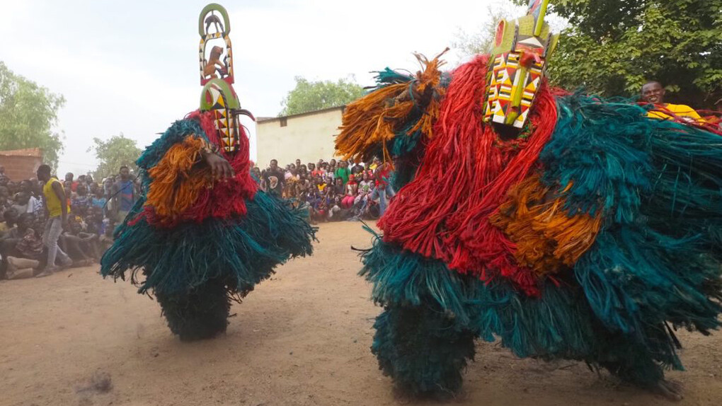 Headpiece carved by David Sanou in the studio of André Sanou, A pair of Kimi masks performing greetings with the lead griot Tchiedo playing his drum behind them, Bindougosso district, Bobo-Dioulasso, Burkina Faso, May 3, 2022. Courtesy of NOMA