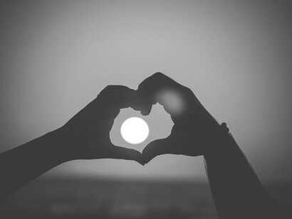 Duas mãos formam um coração no pôr-do-sol