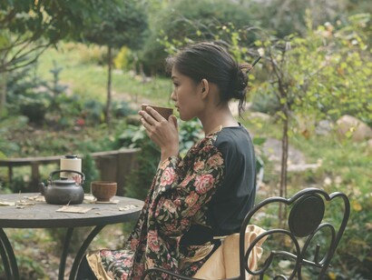 A woman in a tea garden blowing on her cup of hot tea