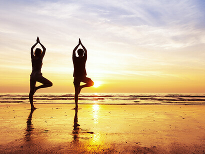 Duas pessoas praticam yoga na beira do mar