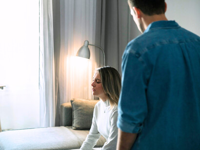 A grieving mother seated in stillness as her partner stands guard over her pain, representing love standing helpless before loss