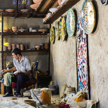 An artisan in Gijduvon, Bukhara Region, Uzbekistan, carefully decorating clay pottery in his traditional workshop