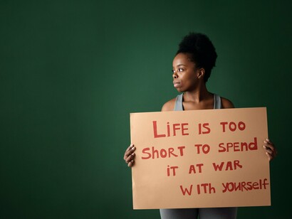 Woman with a sign 'life is too short to spend it at war with yourself'