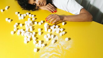 Jovem deitada diante de cubos de açúcar. O açúcar já teve vários grandes centros de disseminação e produção, como Veneza, onde pode ter chagado pelas mãos de cavaleiros que voltavam das cruzadas; a Ilha Da Madeira, graças ao visionário infante D. Henrique; e Pernambuco, estes e outros enviavam o ouro branco para os quatro cantos do planeta