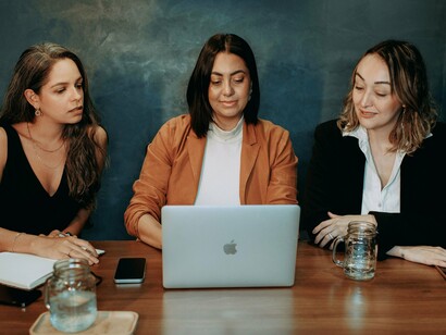 Women sharing ideas around a laptop during a work meeting, reflecting the collective effort and human connection behind meaningful work