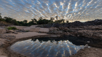 Reflejo de nubes grises y blancas fibrosas en un estanque en una playa de Don Khon al amanecer, Si Phan Don, Laos