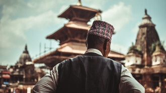A Nepali man stands in the foreground, gazing at the majestic temple in Patan, Nepal, surrounded by the rich cultural architecture of the ancient city
