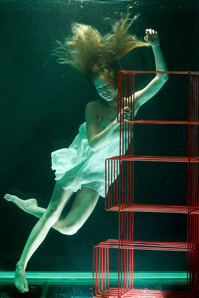 A woman in water, gazing upwards towards a red bookcase, embodying digital surrealism