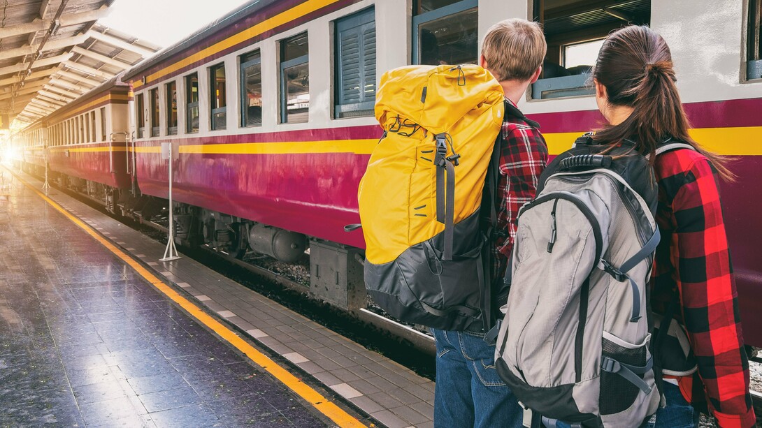 Um homem e uma mulher esperam pelo trem em uma estação, prontos para seguir viagem. Sair do lugar que conhecemos é também um exercício de humildade diante de outras paisagens, culturas e formas de viver