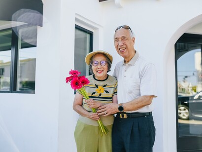 An older couple smiling, with the woman holding some flowers 