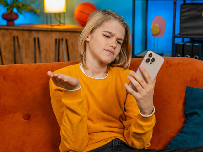 Frustrated teenage girl sitting on a sofa at home, stressed by notification overload after losing an online game on her smartphone