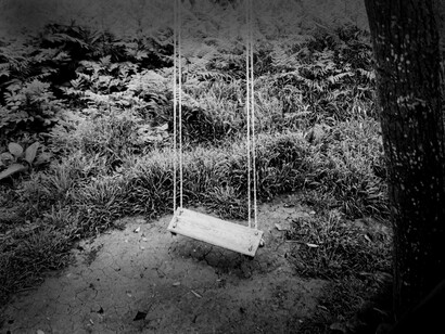 Balanço abandonado em jardim. Na porta para o jardim, lembra-se de uma árvore grande, mas ali nada existia. As memórias estão enevoadas. Ao abrir a porta de rede, um espaço desolado, um jardim moribundo. Olha-o com os olhos semicerrados como se procurasse algo que já não existe. Ao canto, alguém sentado numa cadeira de baloiço