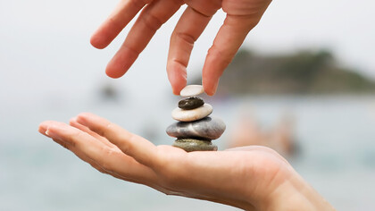 A woman's hands delicately place the final pebble atop a stack of stones, symbolizing completion and mindfulness