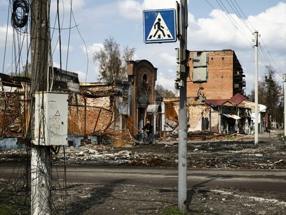 Amid ruins and silence, the faint trace of a pedestrian sign reminds us that life still dares to cross forward