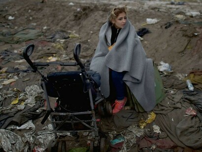 Una refugiada sentada entre basura junto al carrito de su bebé