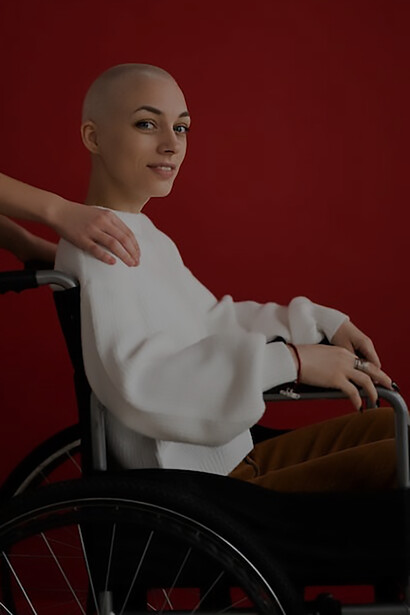 A woman courageously embraces her journey with cancer, radiating positivity as she poses alongside her wheelchair, a symbol of resilience and determination