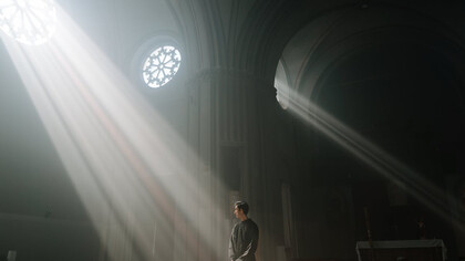 The rays cutting through the darkness serve as a poignant metaphor for the search for truth in a world where faith can be both a refuge and a tool for power 