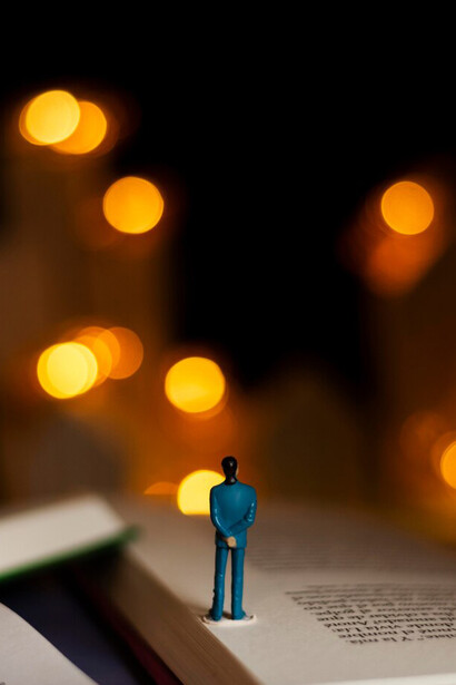A symbolic still life of books and imagination, with a human figure standing atop the literary world