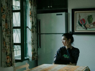 Solitary woman in a dark interior, capturing themes of social isolation, motherhood anxiety, and digital-age tragedy