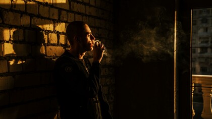 A man leaning against a wall smoking a cigarette 