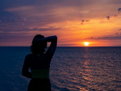 Back view of a woman watching the sunset by the sea