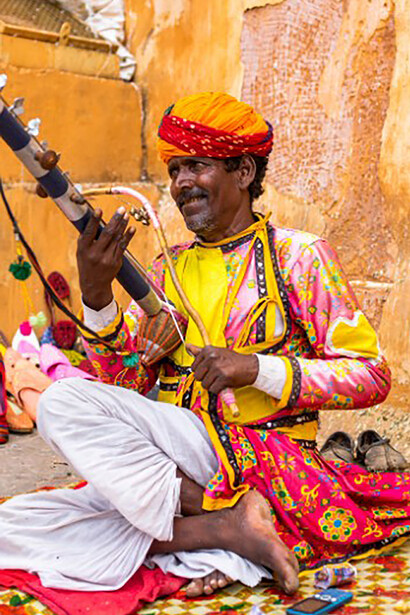 A man, sitting cross-legged on the ground, gently strums a musical instrument, India