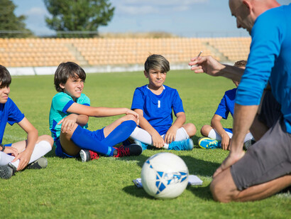 A coach in a blue shirt gives instructions to young athletes on a soccer field