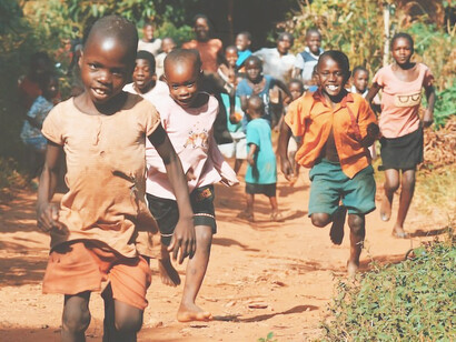 Children running and walking on brown sand surrounded with trees during daytime, Africa