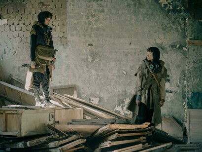 Amid the wreckage of a war-torn building, a man and a woman cling to each other in quiet defiance