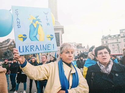 A woman in the streets of London, Uk holding a sign that reads "stand with Ukraine"