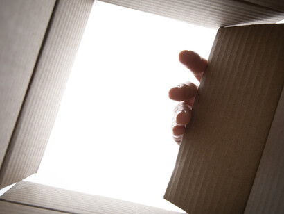 L'apertura di una scatola di cartone vista dall'interno, con una mano che solleva il coperchio, rivelando una luce intensa e misteriosa dall'alto