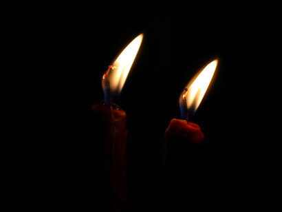 Two candles dimly illuminate a dark picture