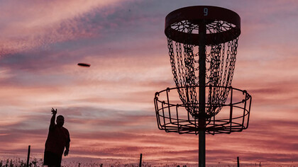 A silhouette of a man throwing a disc toward a disc golf basket
