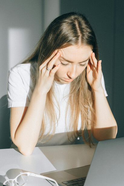 Exhausted from hours of screen time, a young woman holds her glasses in a brightly lit office, highlighting the physical strain of life in a hyperconnected digital environment