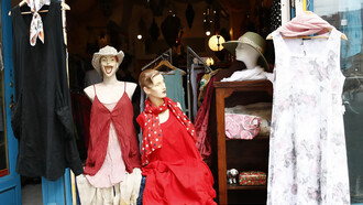 A pair of mannequins displayed in a shop window, showcasing quirky styles in a charity shop that promotes second-hand shopping and sustainable fashion