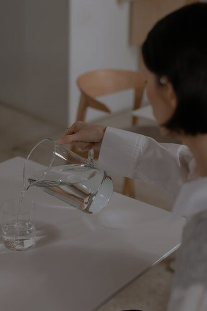 A woman is elegantly filling a glass from a jug with water