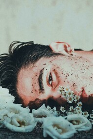A man lies down next to daisies, looking upset